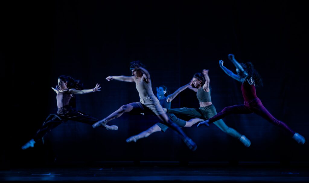 Group of contemporary dance students leaping together on stage