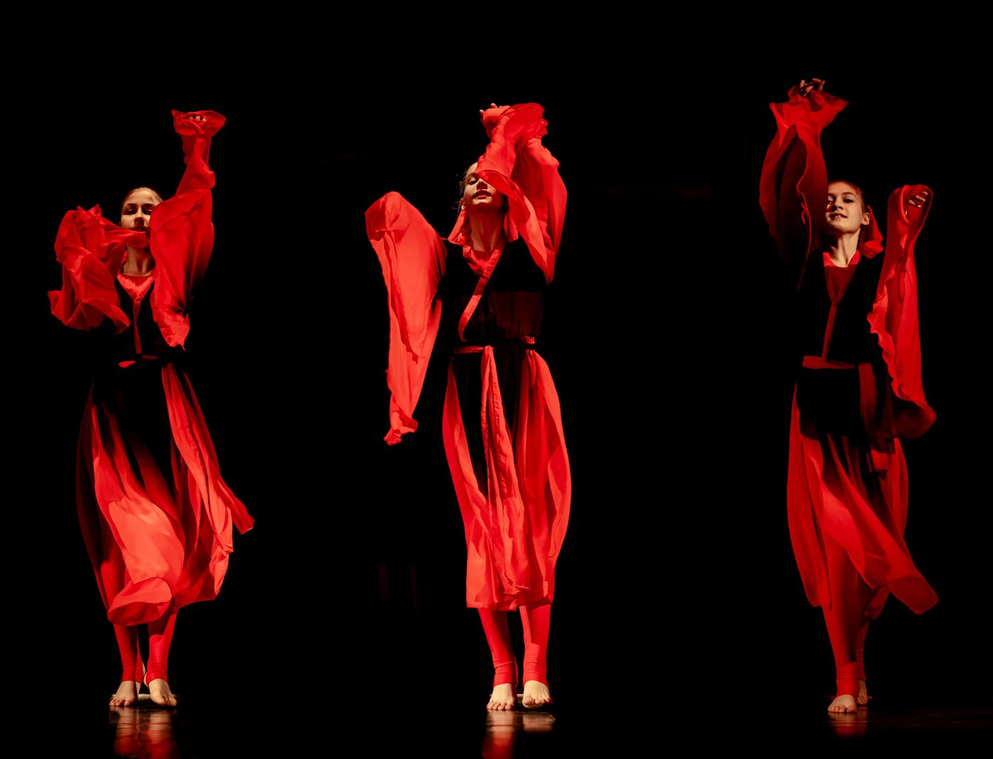 Three dancers performing on stage in vibrant red costumes